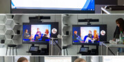Auf einem Bildschirm wird das Girls Day-Interview während eines Videoanrufs angezeigt. Unten sehen zwei junge Frauen das virtuelle Interview in einer modernen Büroumgebung und nehmen daran teil.