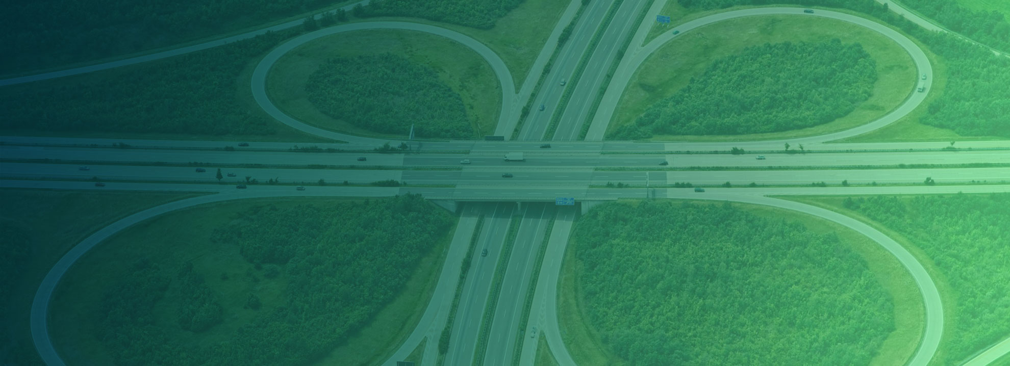 Aerial view of a highway cloverleaf interchange surrounded by greenery, showing multiple lanes and overpasses with some vehicles on the roads.