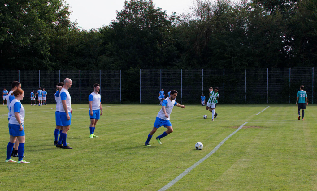 A soccer player in a blue and white uniform prepares to kick off, while teammates and opponents stand ready on the grassy soccer field.