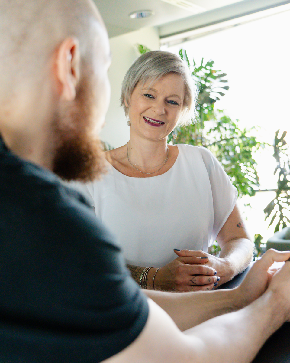 A woman with short gray hair smiles while sitting across from a bearded man in a casual indoor setting with plants in the background, engaging in a conversation about career development for IT leaders.