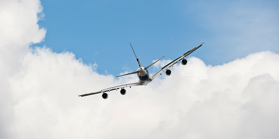A large commercial airplane, maintained through expert MRO, banks to the left in flight against a backdrop of blue sky and white clouds.