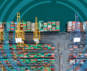Aerial view of a busy shipping port with rows of colorful cargo containers and several large cranes by the water. Blue digital circles, referencing Carbon Border Adjustment Mechanism (CBAM) measures, are overlaid on the image.