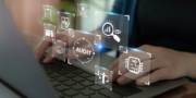 Hands typing on a laptop keyboard with digital icons overlayed, including magnifying glass, cloud, scale, and the word AUDIT, representing data analysis and auditing concepts.