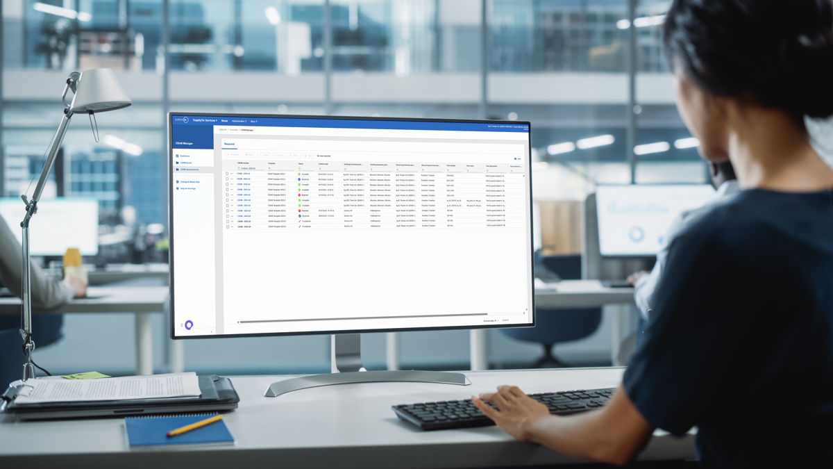 Person working at a desk in a modern office, viewing a data management or spreadsheet software on a large computer monitor.