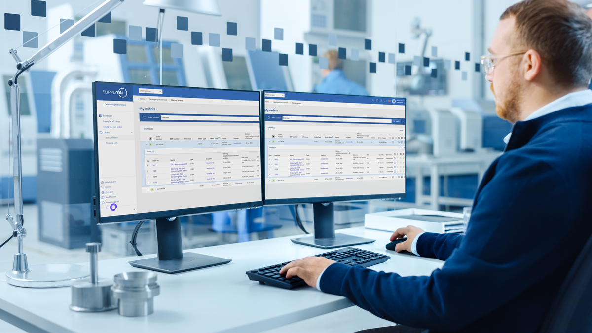 A person at a desk works on two computer monitors displaying data tables in a modern office with industrial equipment in the background.