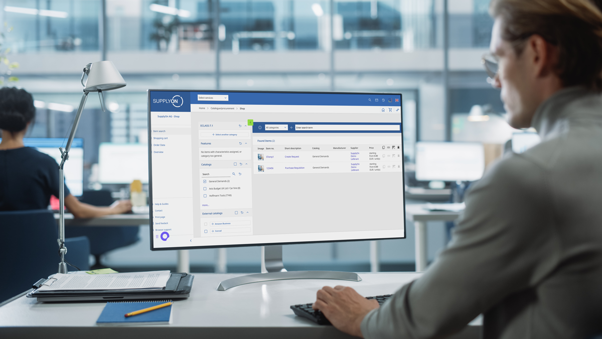 Person working at a desk with a desktop computer displaying a supply chain management software interface in a modern office setting.