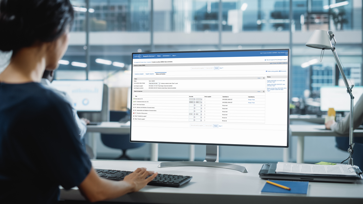 A person sits at a desk in an office, looking at a computer monitor displaying a web-based data management interface.