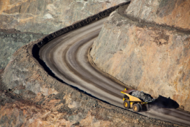 A large dumper truck carrying rocks drives up a winding dirt road inside an open-cast mine.