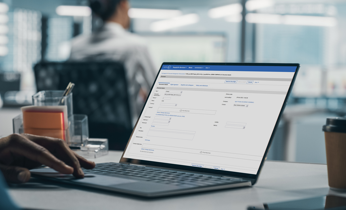 A person uses a laptop displaying a business or financial software form in an office setting, with another person working in the background.