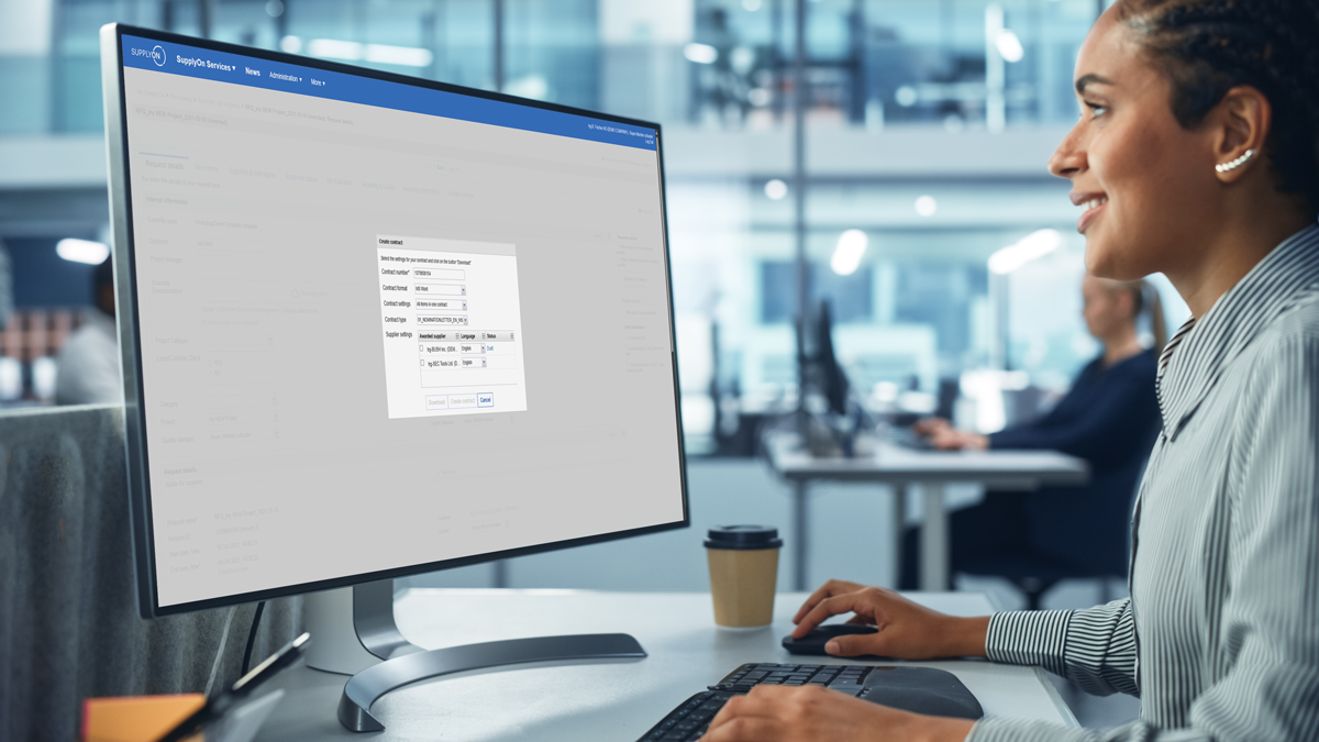 A person works at a desk in an office, using a computer with a data input form open on the monitor.