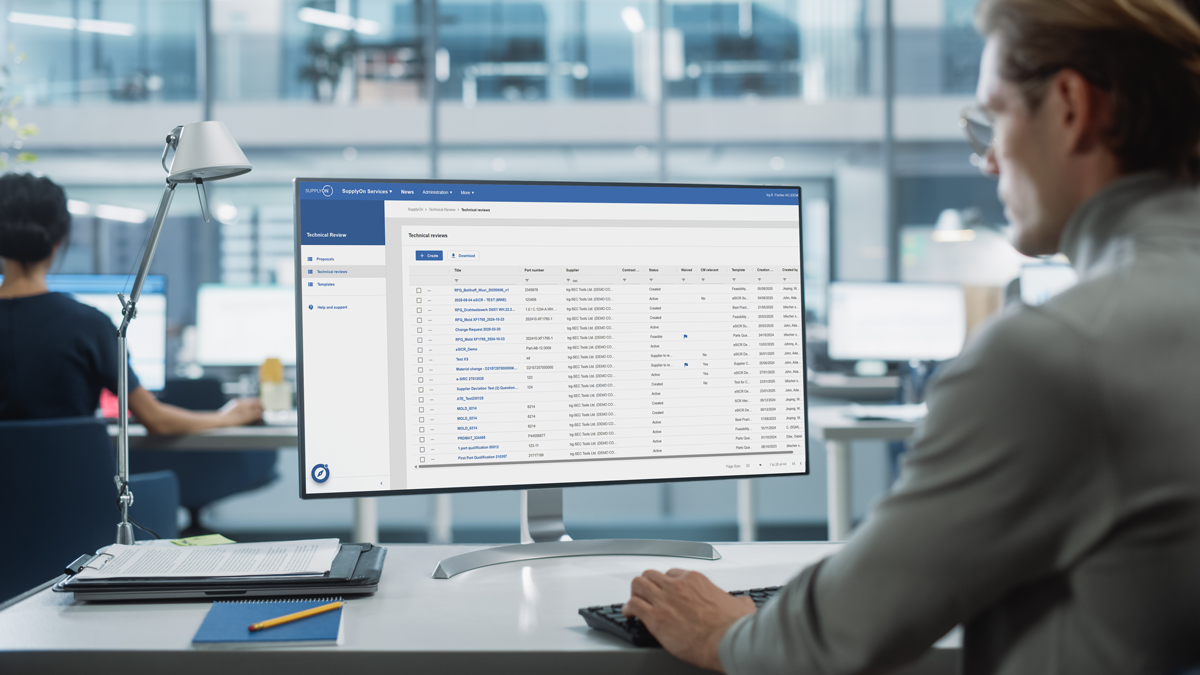 A person sits at a desk working on a computer displaying a database or spreadsheet in a modern office environment.