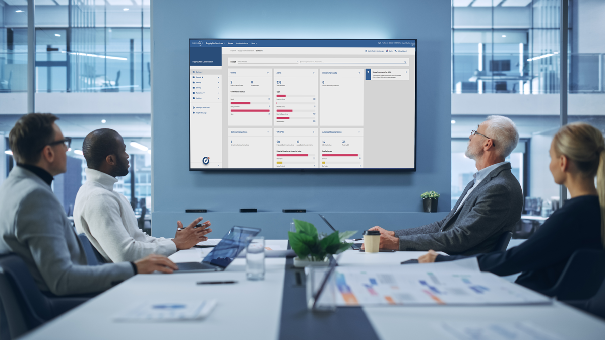 Four people seated at a conference table look at a large screen displaying business analytics and charts in a modern office meeting room.