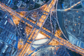 Aerial view of a complex motorway interchange with multiple flyovers and heavy traffic, surrounded by urban buildings and construction sites.
