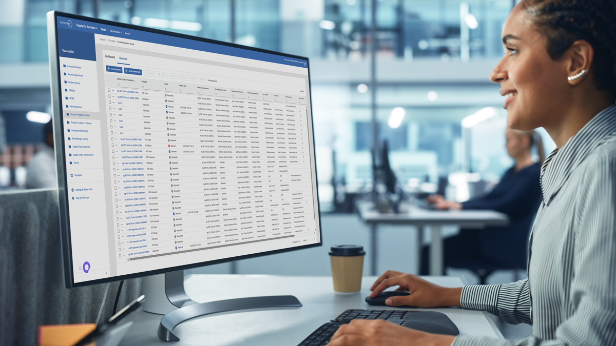 A person sits at a desk using a desktop computer displaying a detailed spreadsheet or data management software in an office setting.