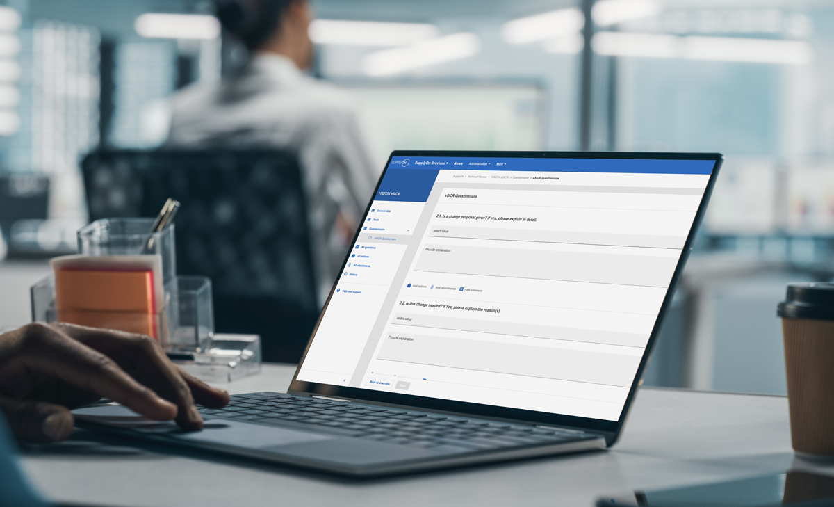 A person uses a laptop displaying an online forum or messaging platform in an office setting, with another person blurred in the background.