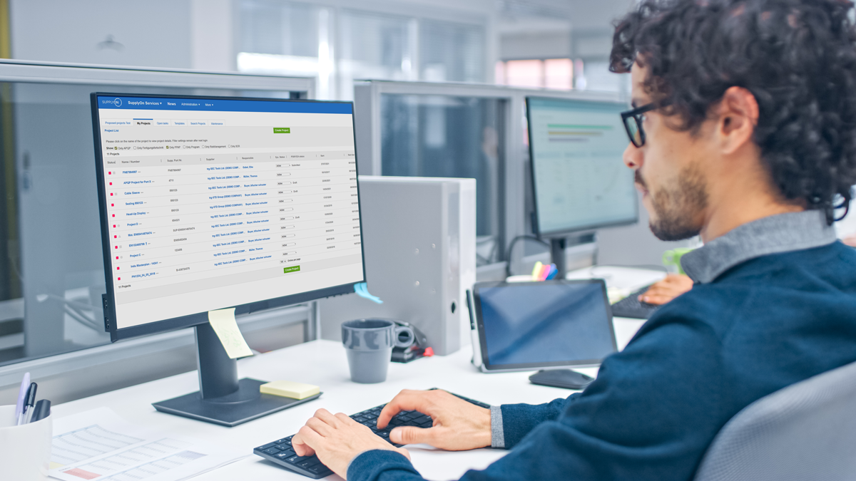 Man sitting at a desk in an office, working on a computer displaying a dashboard with a table of data and various flags.