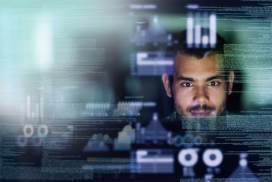 A man looks at a computer screen displaying digital data, graphs, and code overlays in a dark environment.