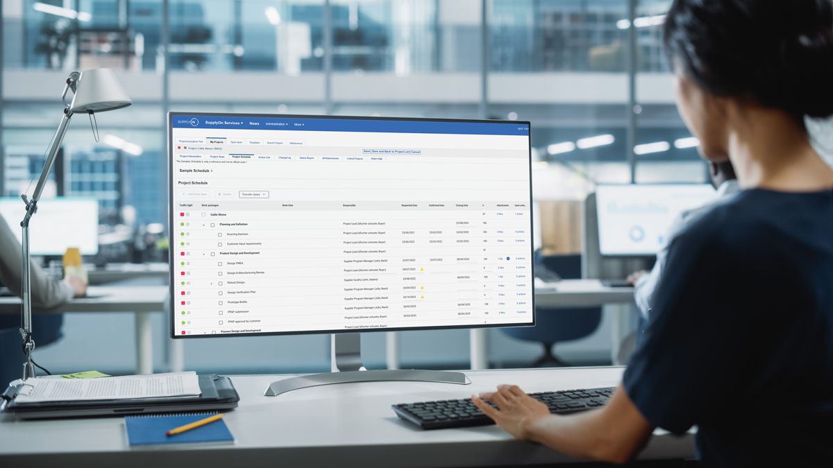 Person working at a desk in a modern office, viewing a computer monitor displaying a project management dashboard with tasks and statuses.