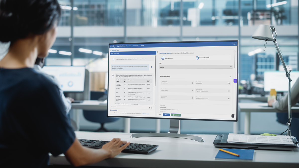 Person working at a desk, viewing a large computer monitor displaying a dashboard with forms and data in an office setting.