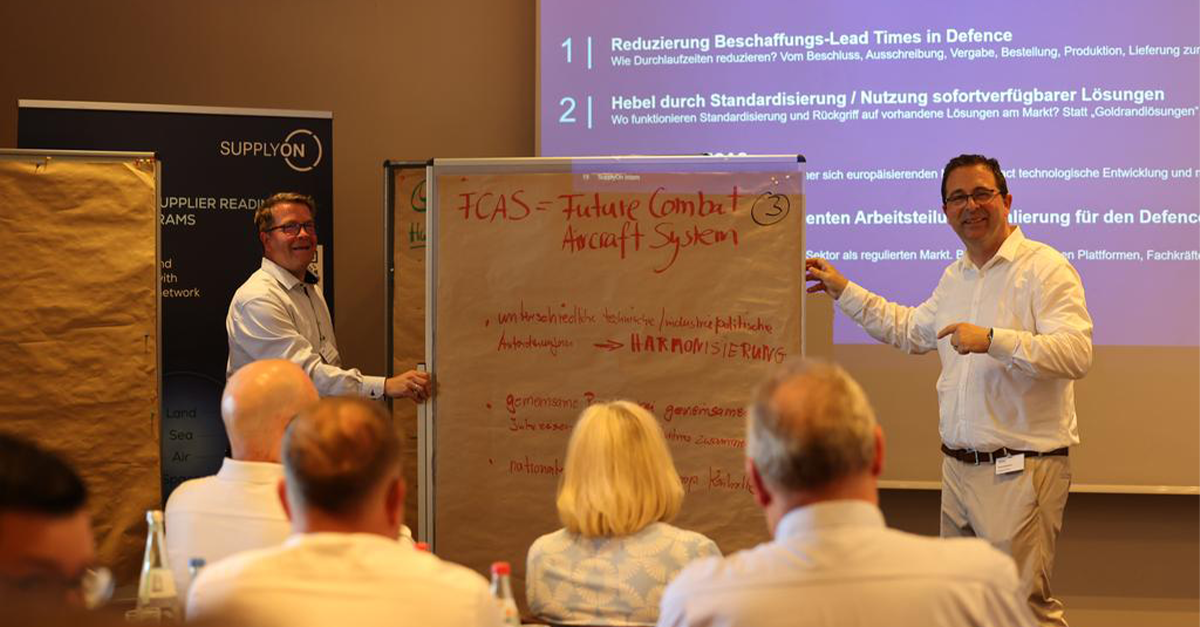 Two presenters stand by a flipchart with FCAS—Future Combat Aircraft System written on it, addressing defence readiness at a professional seminar with projected slides in the background.